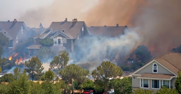 Homes surrounded by thick wildfire smoke with flames visible nearby