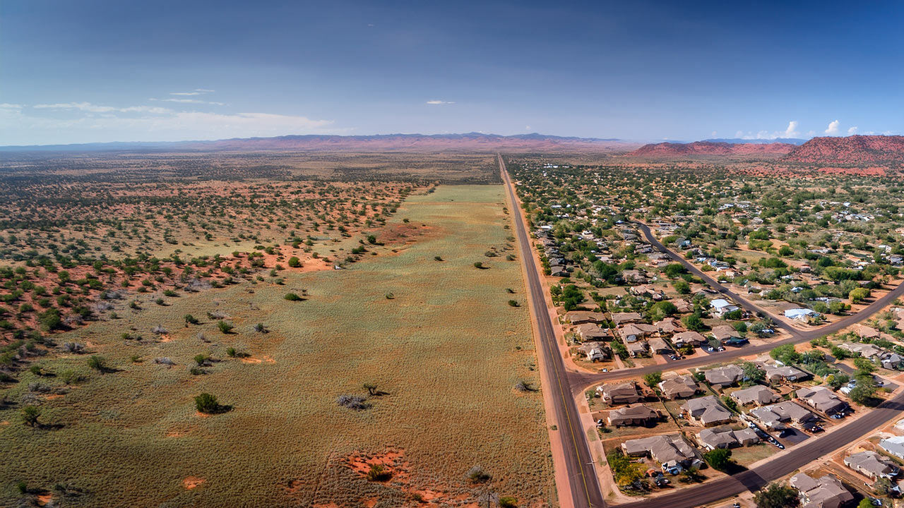 Aerial view of undeveloped public land near a suburban housing development, symbolizing the potential for smarter housing solutions.